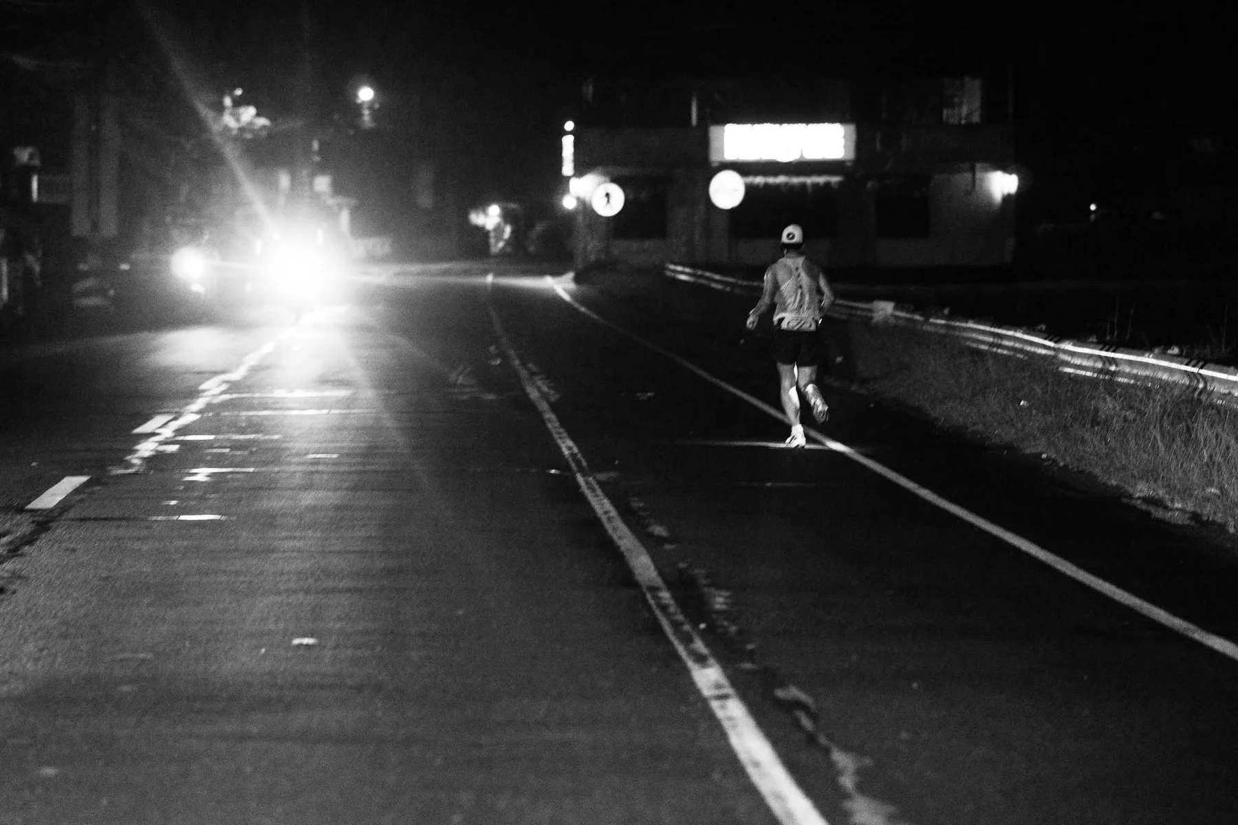 A runner moving alone along a dark road toward bright headlights