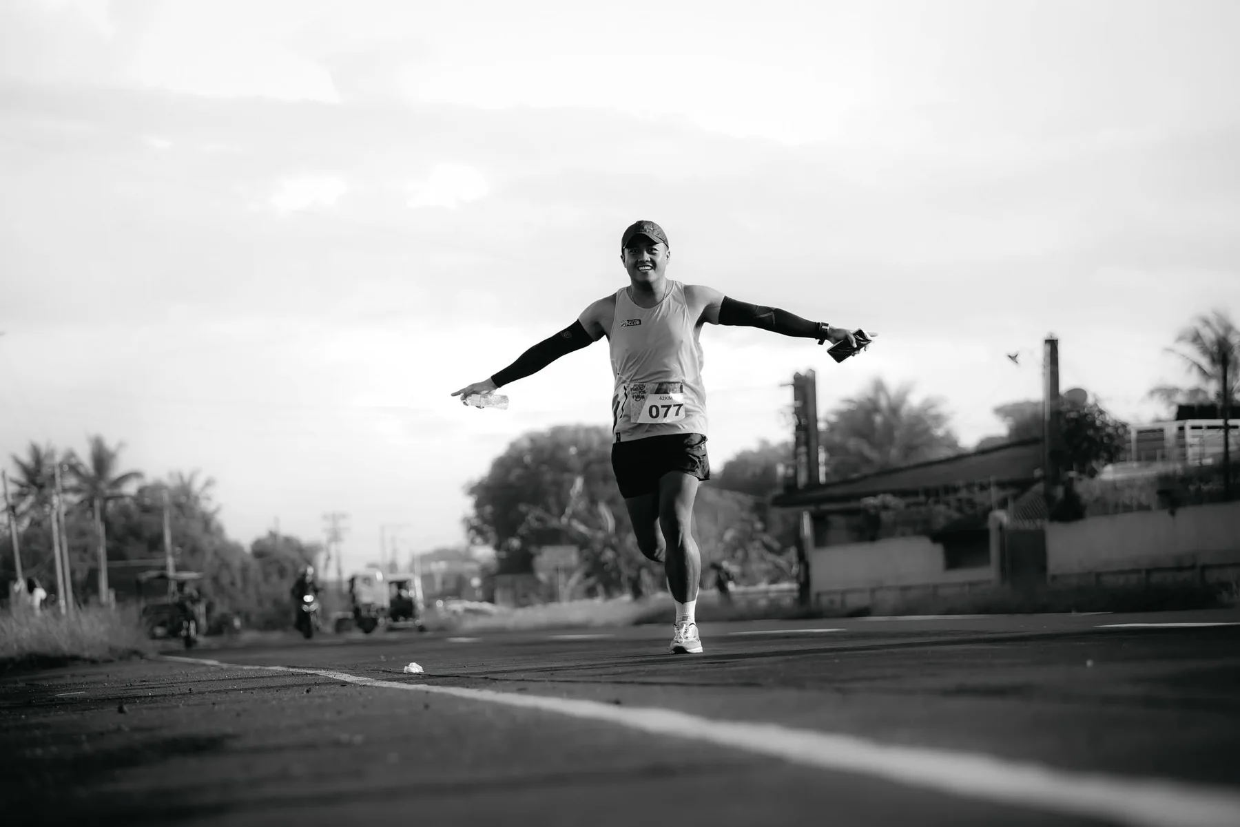 A smiling marathoner running with both arms open after sunrise