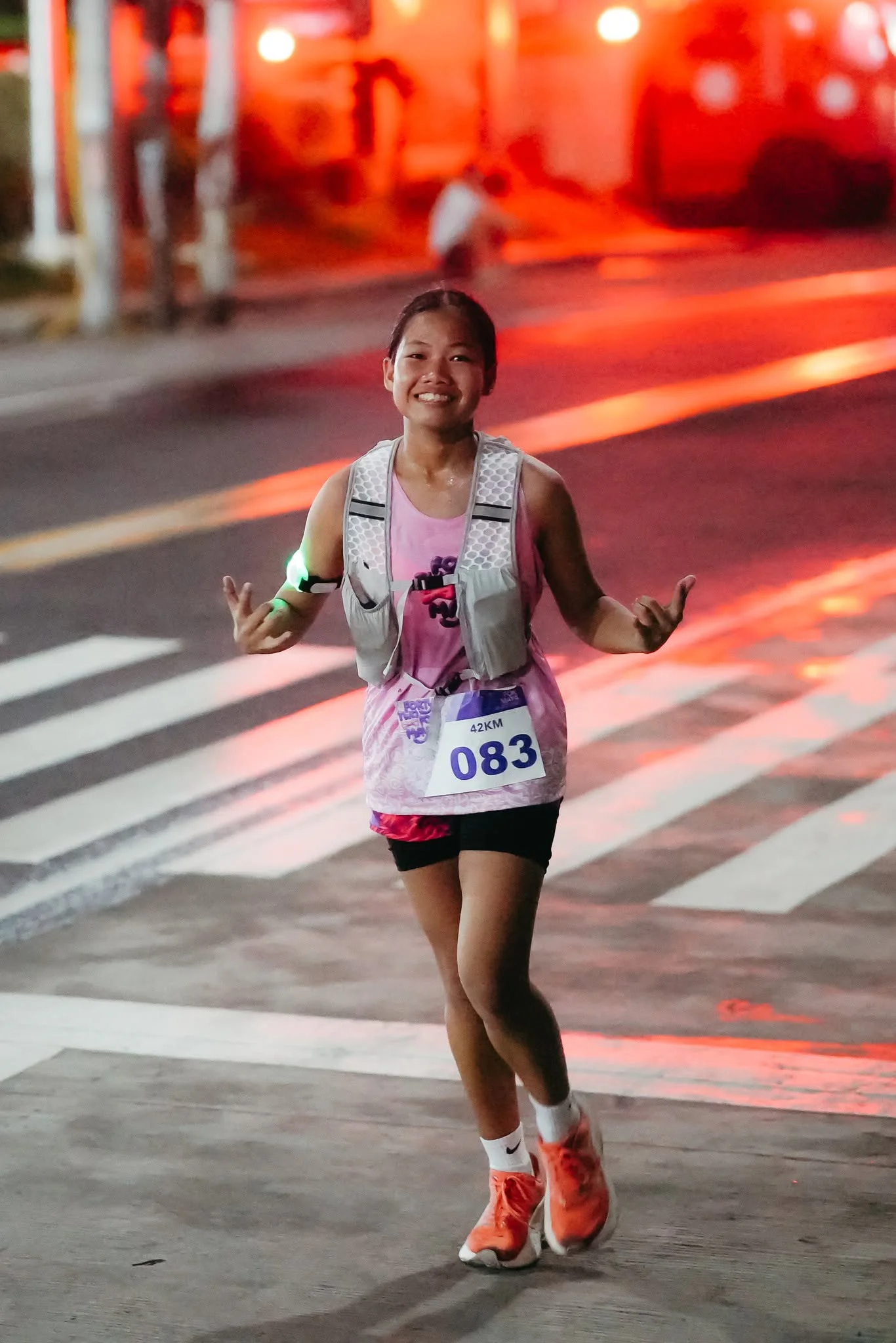 A smiling runner in a pink race singlet giving a hand gesture on the road